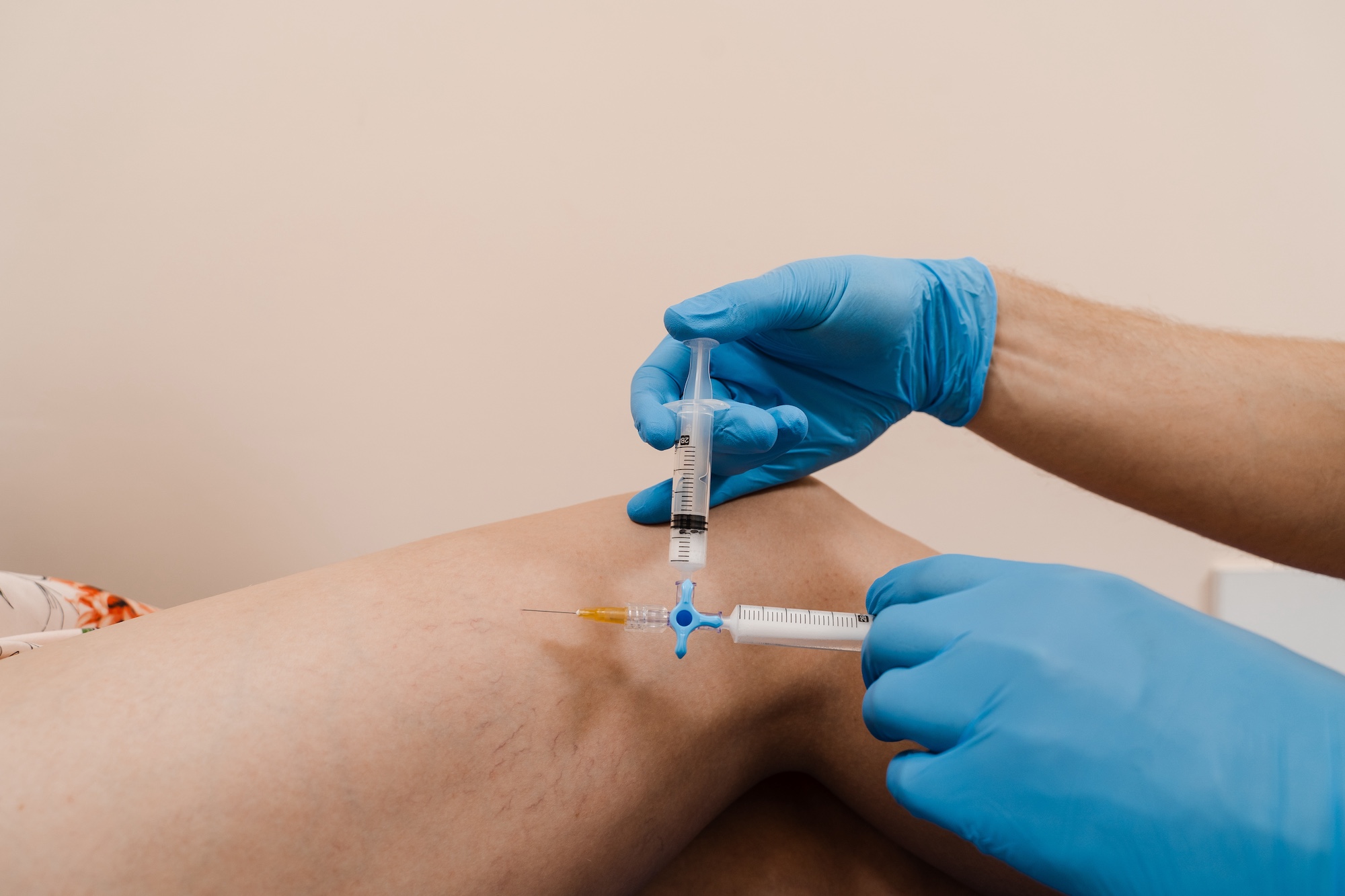 Gloved healthcare worker administering an injection into a patient’s leg with two syringes