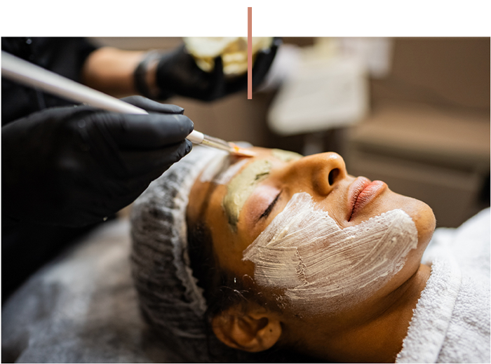 Person receiving a facial with cream mask applied by a gloved esthetician
