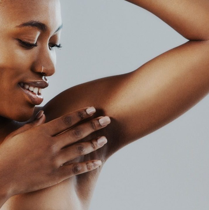 Smiling woman touching her underarm and looking at her skin