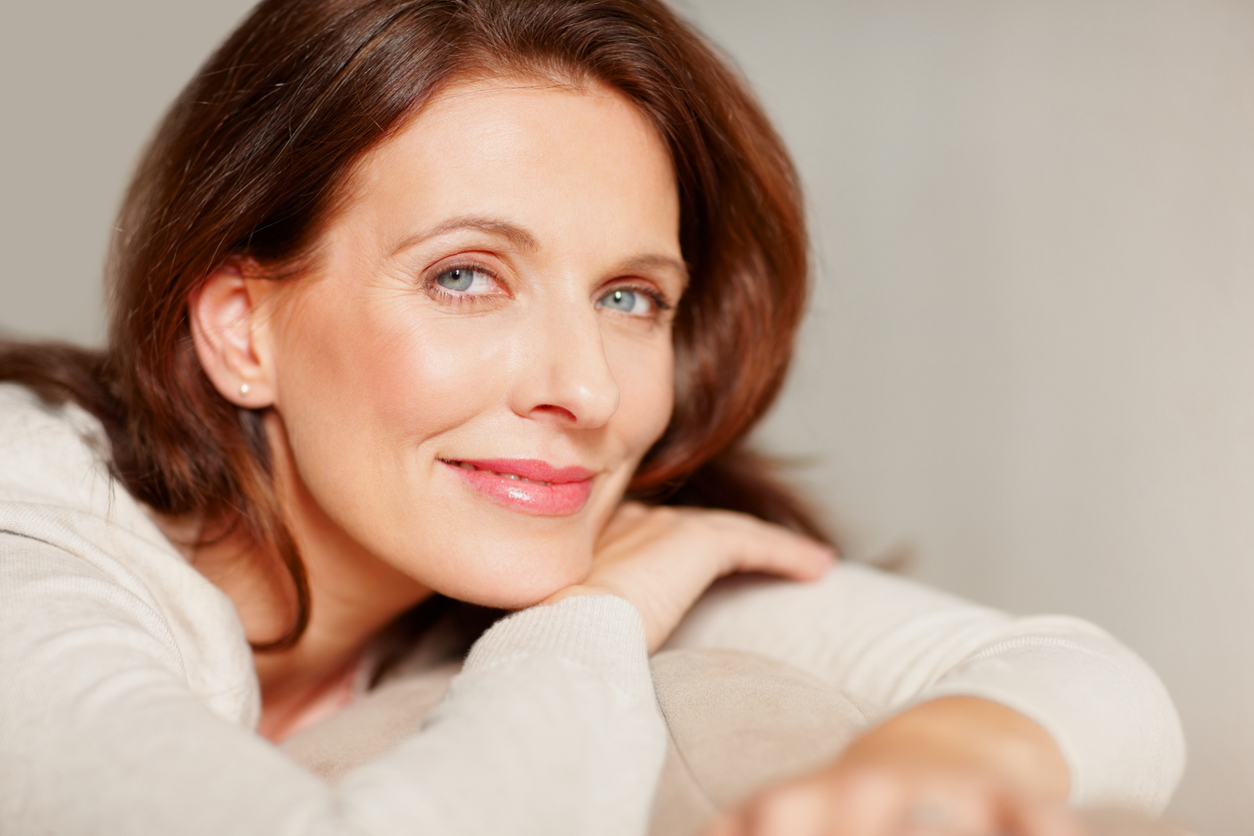 Close-up portrait of a smiling woman with brown hair resting on a sofa