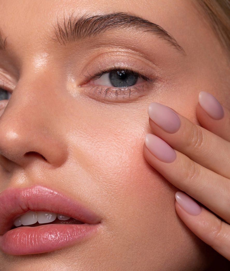 Close-up of a woman’s face with glossy lips, soft makeup, and manicured nails