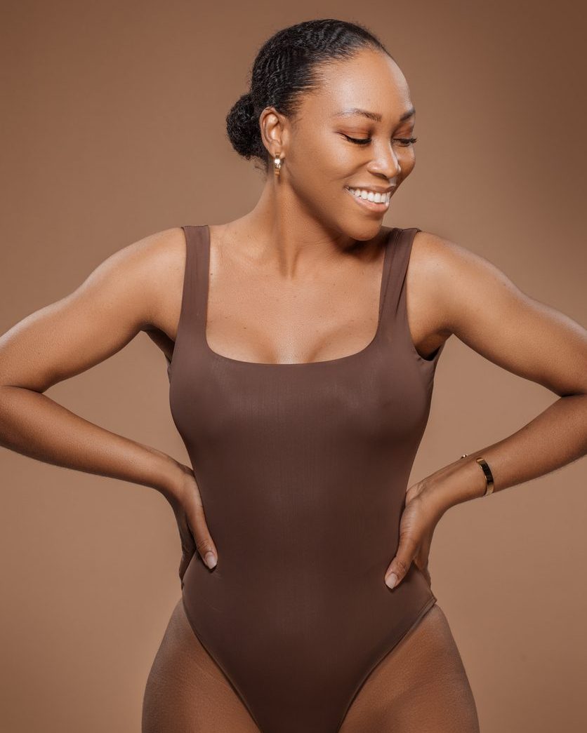 Smiling woman in brown bodysuit posing against beige background