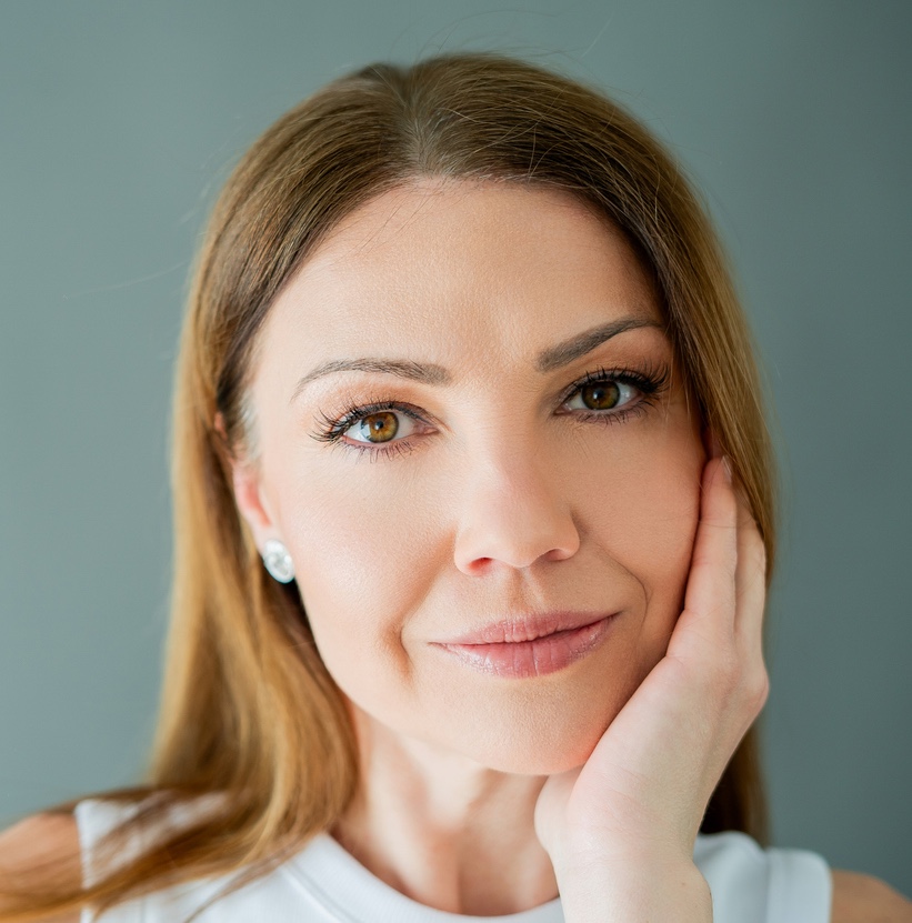 Close-up portrait of a woman with long hair, resting her hand on her face against a gray background