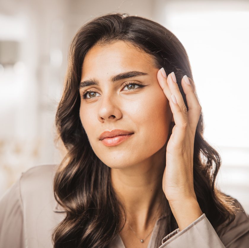 Portrait of a woman with dark hair touching her face in soft natural light